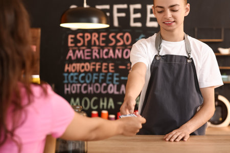 Young male barista receiving payment from visitor in cafeの写真素材