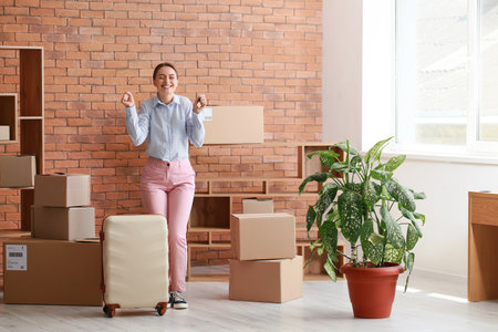 Happy young woman with key and suitcase in her new flat