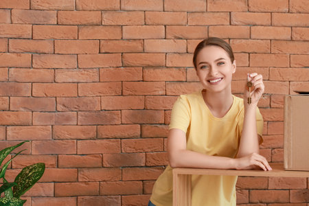 Happy young woman with key from house near brick wallの写真素材
