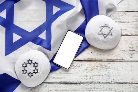 Mobile phone, kippahs and flag of Israel on light wooden backgroundの写真素材