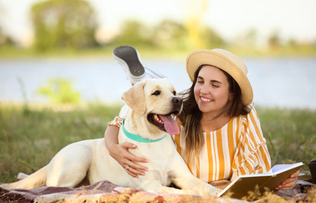 Woman with cute Labrador reading book outdoors on summer dayの写真素材