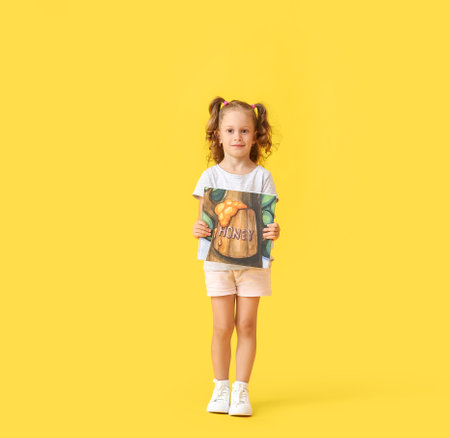 Adorable little girl with book on yellow backgroundの写真素材