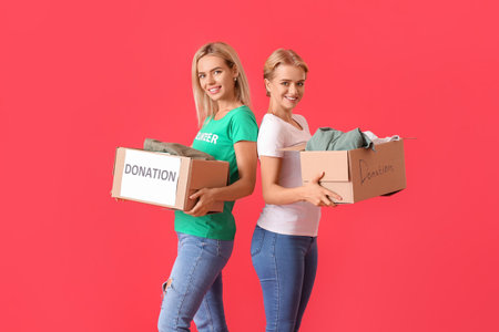 Young women holding boxes with clothes for donation on red backgroundの写真素材