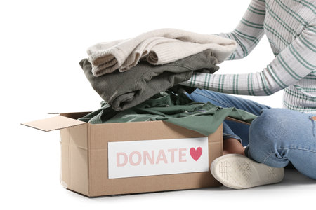 Young woman putting donation clothes in box on white backgroundの写真素材