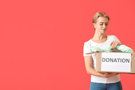 Young woman holding box with donation clothes on red backgroundの写真素材