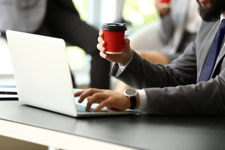 Man drinking coffee while working on laptop in office, closeupの写真素材