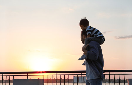 Father carrying his little son near river at sunsetの写真素材