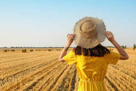 Romantic young woman in hat on harvested field background