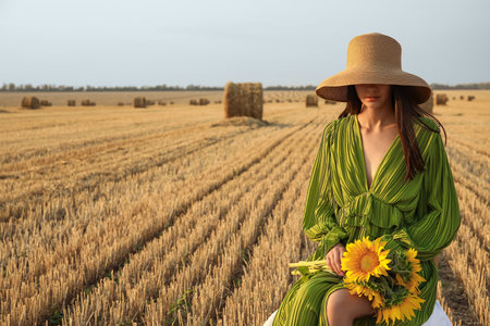 Romantic young woman with sunflowers on harvested field backgroundの写真素材