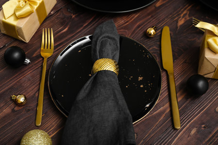 Beautiful table setting with black plate, Christmas balls and gifts on wooden backgroundの写真素材