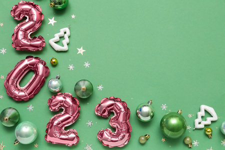 Figure 2023 made of balloons, Christmas decorations and confetti on green background