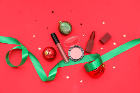 Makeup products with Christmas balls and ribbon on red backgroundの写真素材