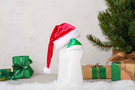 Bottles of detergent with Santa hat on snow against light wall, closeupの写真素材