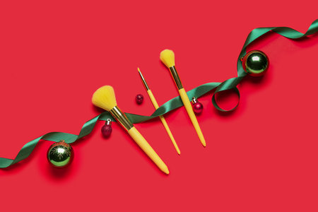 Makeup brushes with Christmas balls and ribbon on red background