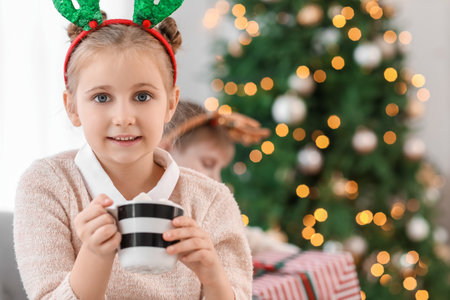 Little girl in reindeer horns with cup of cocoa at home on Christmas eveの写真素材
