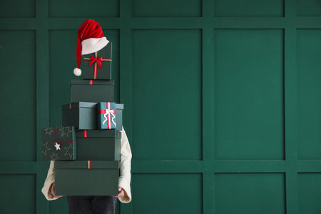 Woman with Christmas presents and Santa hat near green wall