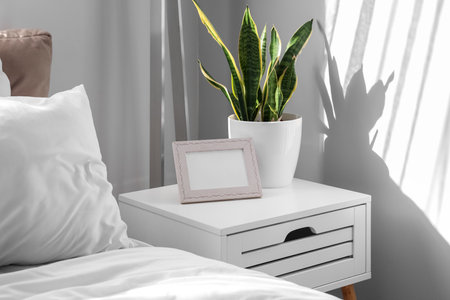 Bedside table with photo frame and houseplant in light bedroomの写真素材