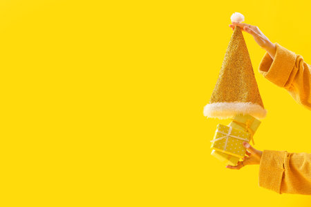 Woman with Christmas gift boxes and Santa hat on yellow backgroundの写真素材