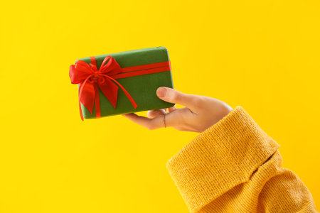 Woman with Christmas gift box on yellow backgroundの写真素材