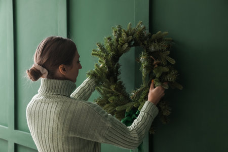 Woman hanging Christmas wreath on color wallの写真素材