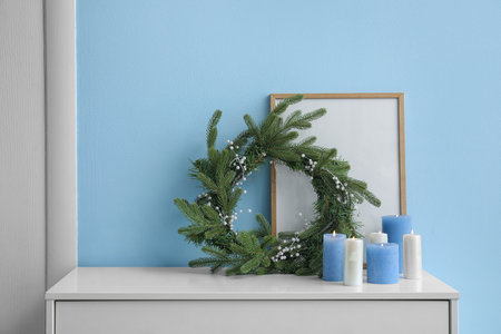 Christmas wreath, burning candles and blank picture frame on table near color wallの写真素材