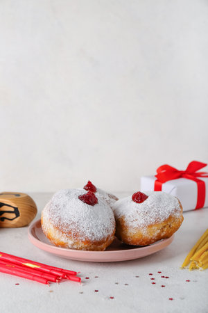 Plate with tasty donuts, dreidel, candles and gift for Hannukah celebration on white backgroundの写真素材