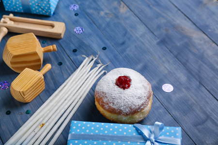 Tasty donut with dreidels, candles and gifts for Hannukah celebration on blue wooden backgroundの写真素材