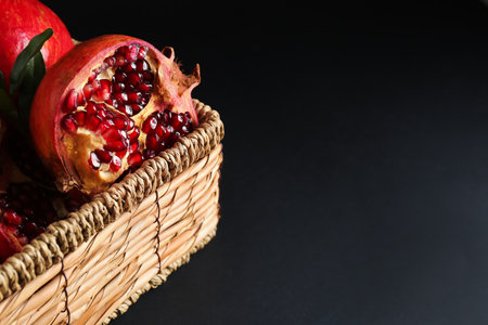 Wicker basket with fresh pomegranates on dark background