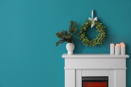 Fireplace with fir branches in vase, candles and Christmas mistletoe wreath on blue wallの写真素材