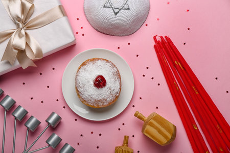 Plate with donut, candles, Jewish hat, menorah and gift for Hanukkah celebration on pink backgroundの写真素材
