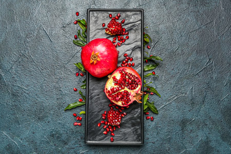Composition with fresh pomegranates, seeds and plant leaves on dark color backgroundの写真素材