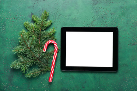 Modern tablet computer, candy cane and fir branch on color background