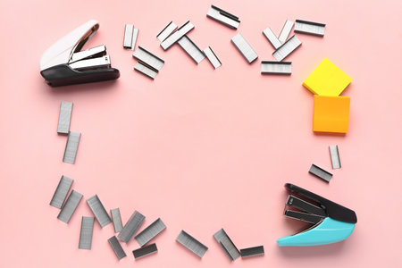 Frame made of staplers and staples on pink background