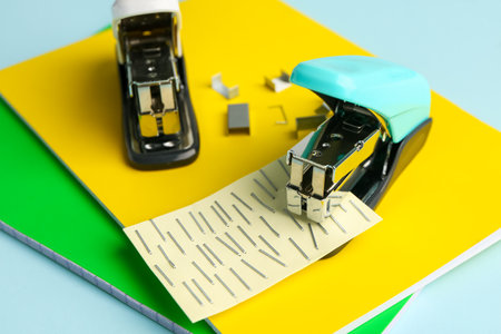Notebooks and staplers on color background, closeup