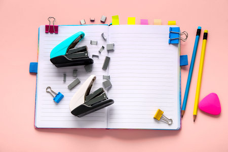 Set of stationery with staplers and notebook on pink background