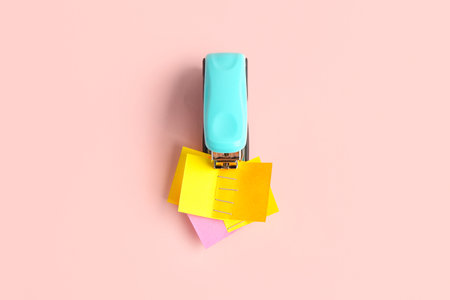 Office stapler with sticky notes on pink background