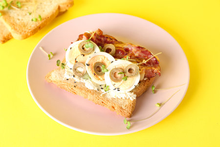 Plate of delicious toast with boiled egg and fried bacon on yellow background, closeup