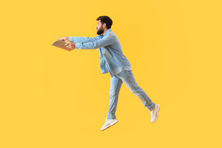Handsome bearded man with clipboard jumping on yellow backgroundの写真素材