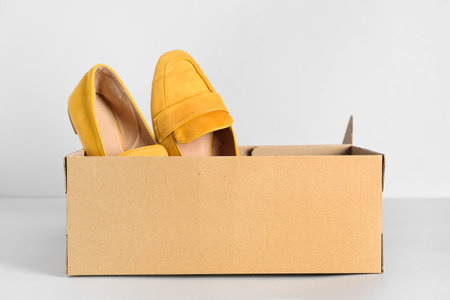 Cardboard box with yellow loafers on light background