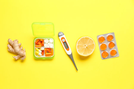 Pills for sore throat, ginger, lemon and thermometer on yellow backgroundの写真素材