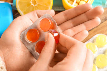 Woman taking pill for sore throat on wooden background, closeup