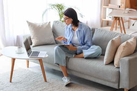 Female psychologist video chatting with patient on sofa at homeの写真素材