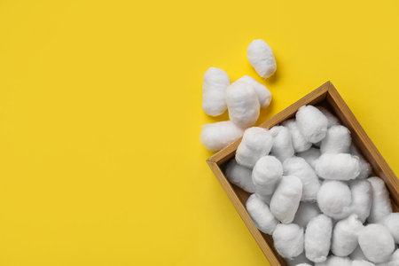 Wooden box of soft cotton balls on yellow backgroundの写真素材