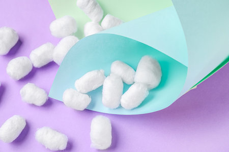Paper sheets with cotton balls on lilac background