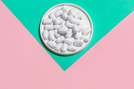Plate of soft cotton balls on color background