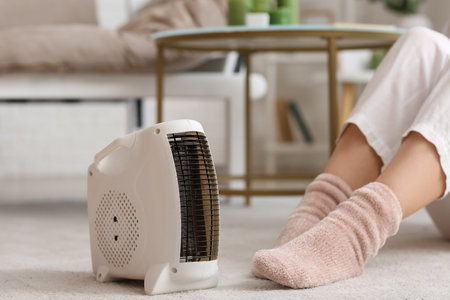 Modern electric fan heater and woman in warm socks on carpet, closeupの写真素材
