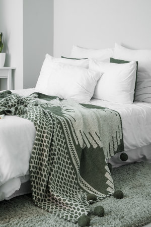 Big bed with cozy pillows near light wall in room