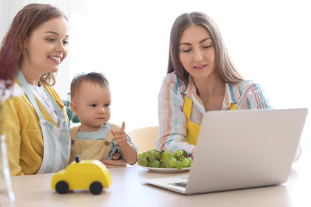 Happy lesbian couple with their little baby and laptop at table in kitchenの写真素材