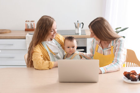 Happy lesbian couple with their little baby and laptop in the kitchenの写真素材