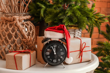 Alarm clock with Santa hat and Christmas presents on table in room, closeupの写真素材